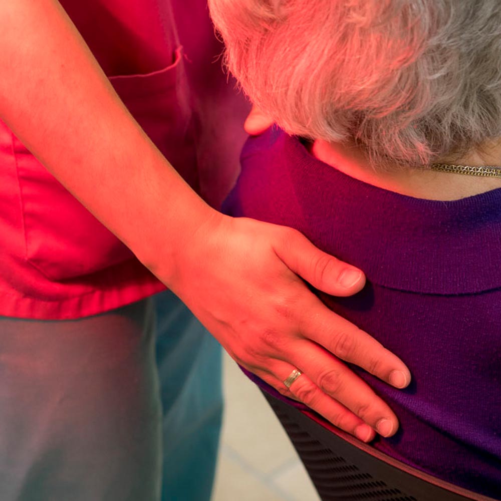 Una trabajadora del centro apoya su mano en la espalda de una residente
